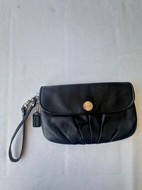 A black leather Coach pleated flap wristlet clutch with logo hardware.